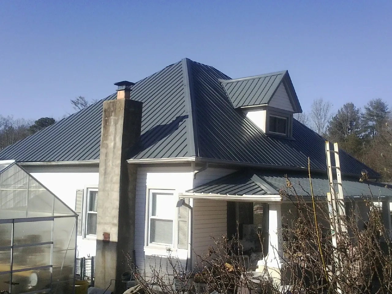 Dark blue standing seam metal roof on a white farmhouse with dormer — Slate & Tile Roof Repair by Roofing Brothers in Britt