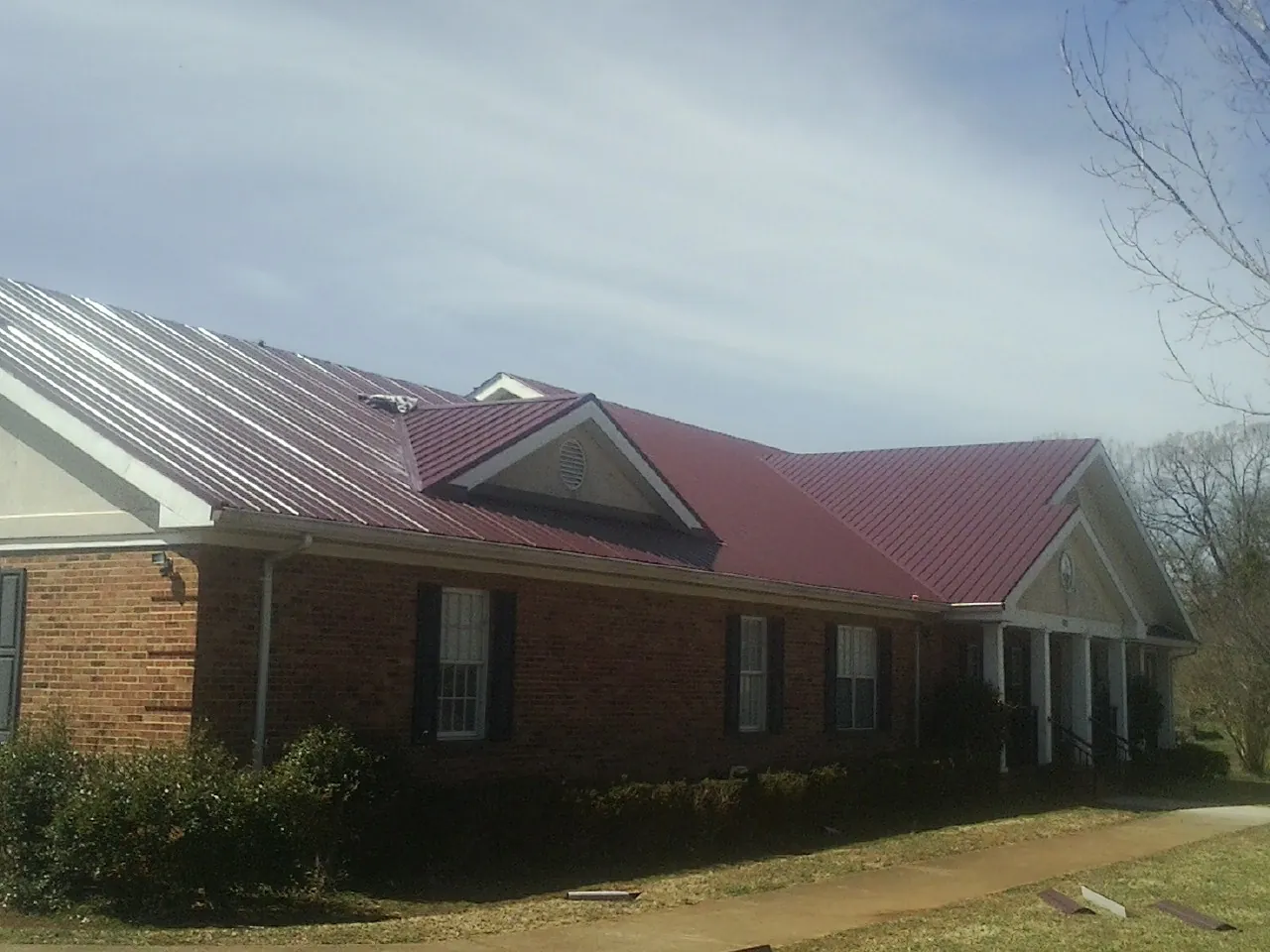 Red metal roof with gabled entries on a long brick building, from a Hail Damage Roof Repair job in Britt