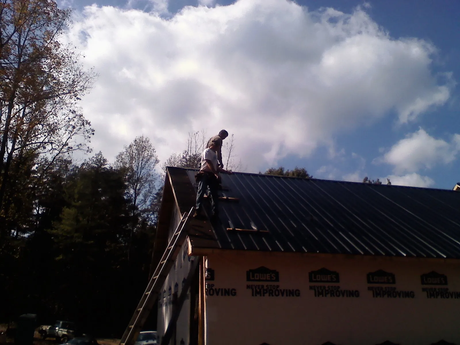 Roofer fastening dark metal panels high against a cloudy sky, from a Roof Inspection job in Britt