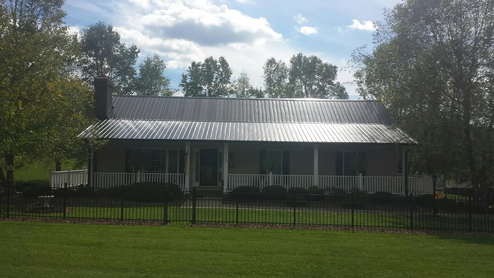Gray metal roof on a brick ranch with a full width front porch — Gutter Guard Installation work by our crew in Britt