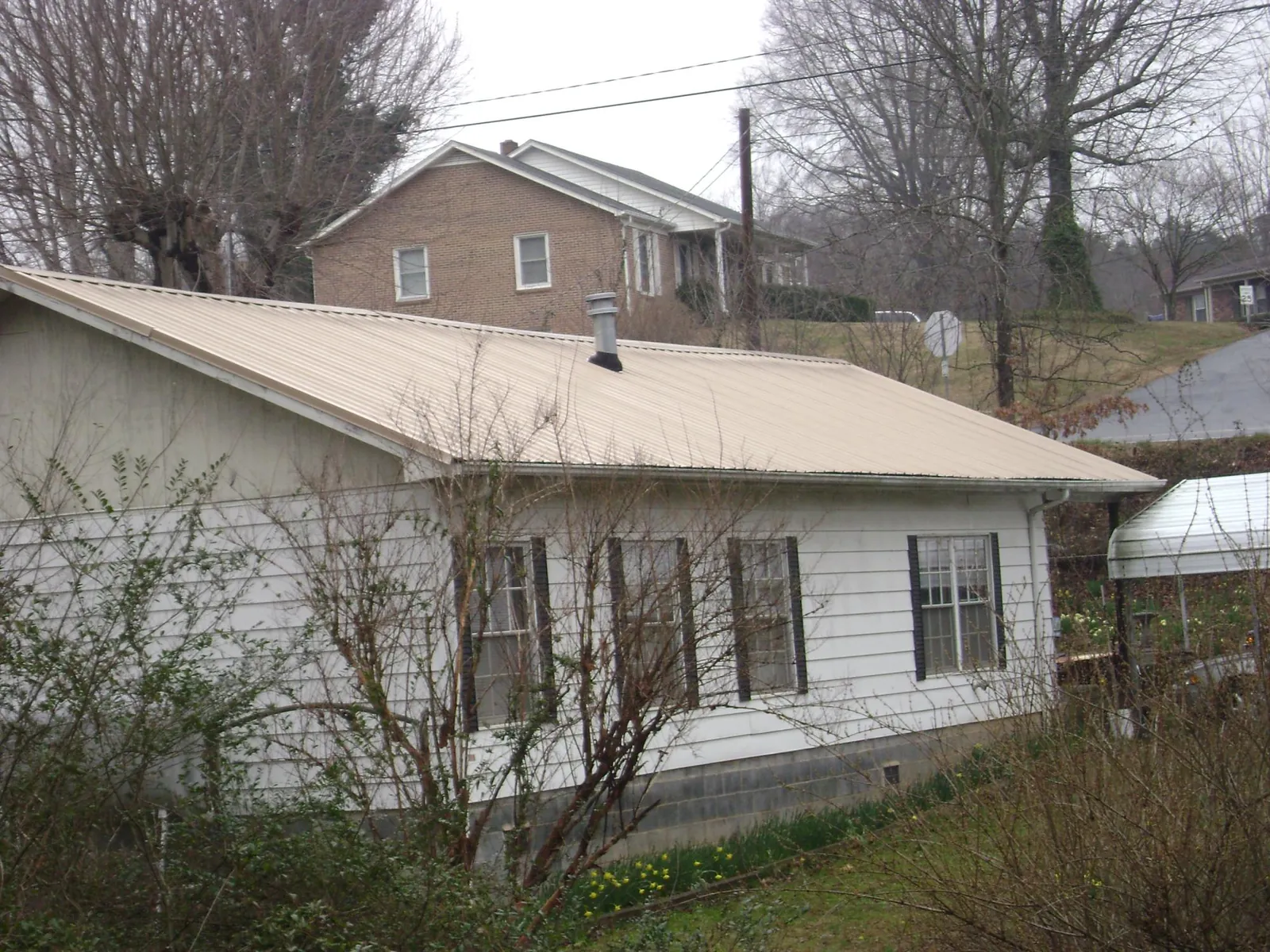 Tan metal roof on a white sided house set into a hillside — Commercial Roofing by Roofing Brothers in Britt