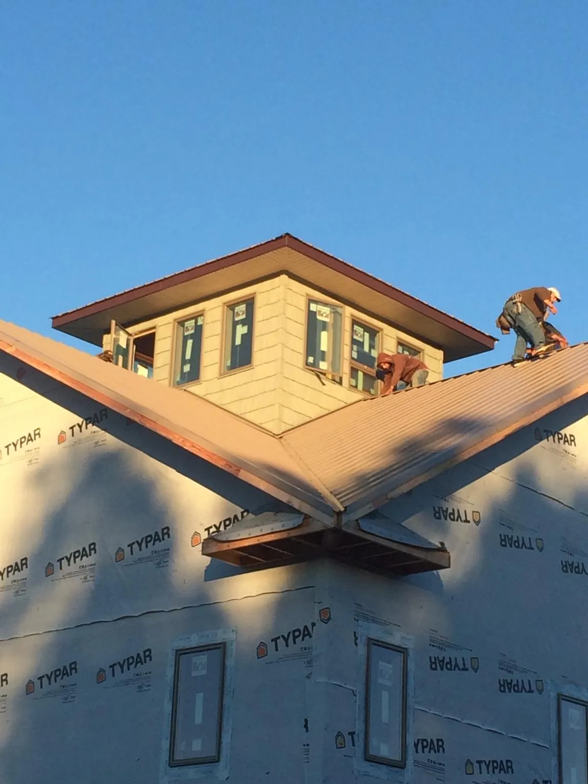 Roofers working around a rooftop cupola on a new metal roof at sunset — Roof Waterproofing in Britt by Roofing Brothers